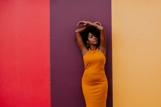 Thoughtful woman with arms raised standing against multi colored wall