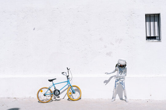 Boy in astronaut costume standing by bicycle on sidewalk in city