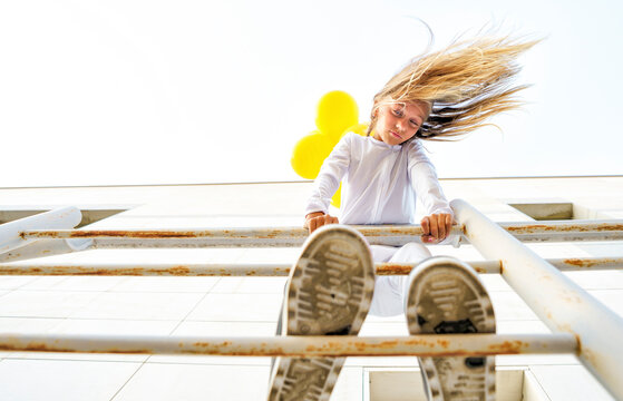 Low angle view of girl standing on railing with tousled hair during sunny day