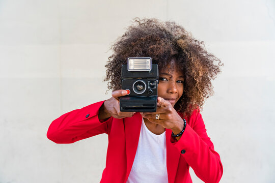 Woman taking picture from camera while standing against white wall