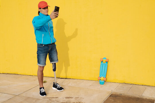 Man wearing cap taking selfie while standing by yellow wall