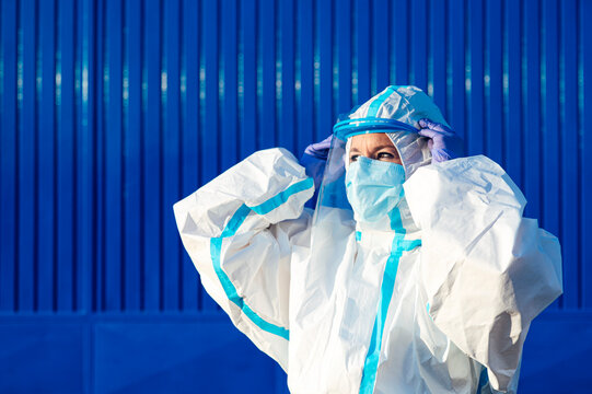 Nurse wearing face shield while standing against blue wall on sunny day