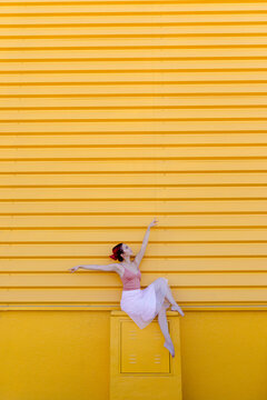 Ballerina with arms raised dancing on seat against yellow wall