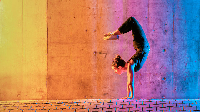 Woman Practicing Gymnastic In Multi Colored Light Against Wall