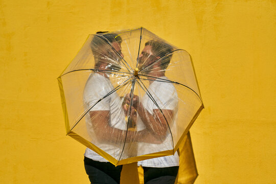 Gay couple holding umbrella while standing against yellow wall