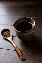Green tea (sencha) in a traditional, japanese tea cup and sencha leaves on a wooden tea spoon. Dark wooden background.	