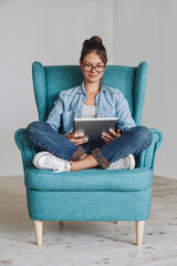 Young woman sitting in the armchair and using tablet, isolated