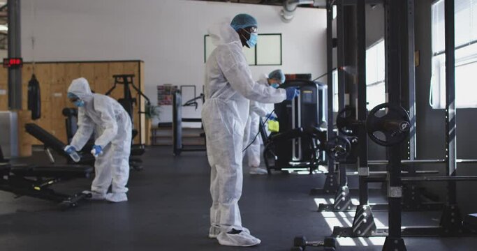 Team of health workers wearing protective clothes cleaning gym by using disinfectant sprayer