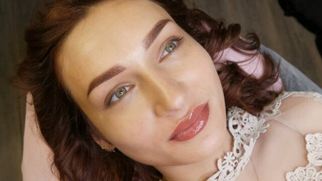 Beautician in black gloves makes permanent makeup correction of the shape of the eyebrows to a young beautiful girl. Microblading, eyebrow tattoo in a beauty salon.