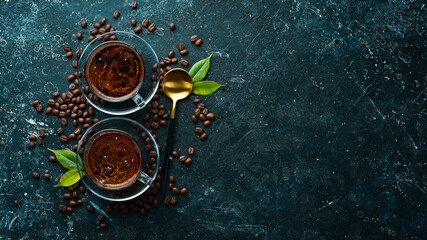 Two cups of fragrant coffee and coffee beans on a black stone background. Top view. Free space for text.