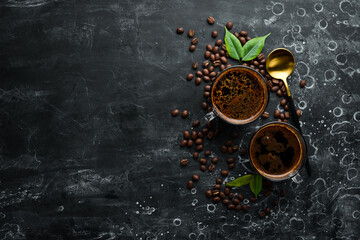 Two cups of fragrant coffee and coffee beans on a black stone background. Top view. Free space for text.