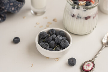 Bowl of fresh blueberries, beautiful spoon and a glass jar of homemade yogurt with berries  on white background. Proper nutrition concept