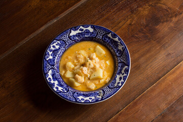 Antique plate decorated with stew cod and potatoes on rustic chestnut wood background. Cooking recipes with fish and vegetables.