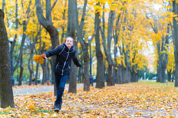 a girl running through the park and enjoys autumn, beautiful nature with yellow leaves