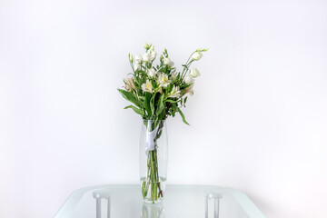 Bouquet of alstroemerias and eustomas in a glass vase on a glass table. Beautiful flowers for women's day. A bouquet as a gift. White green bouquet.