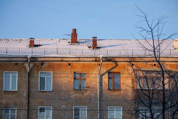 Windows of an old brick house close-up in the rays of the rising sun. Top floor, drainpipe. The roof of the house is covered with snow. Chimneys.