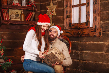 Happy young couple in santa hat at home at christmas with new year gifts