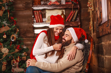 Happy young couple in santa hat at home at christmas with new year gifts