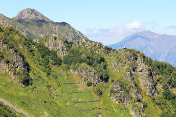 Landscape of green mountain slope on a summer day with snow shields and exploders for avalanches prevention, view from afar