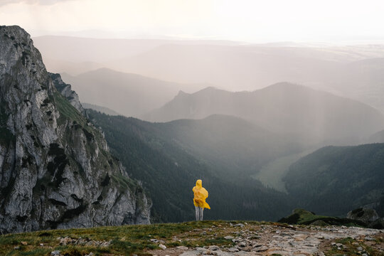 Anonymous tourist in yellow raincoat hiking in mountain during a thunderstorm