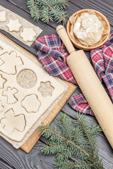Cooking process. Dough, rolling pin. Spruce twigs and napkin on dark wooden background. Cutting shaped cookies by mold