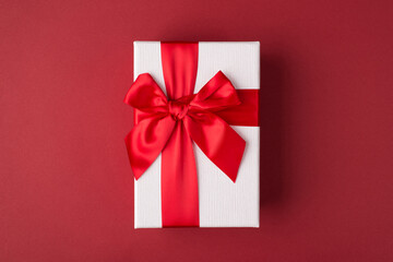 Flatlay close up top above photo of white gift box with red ribbon isolated fashionable burgundy...