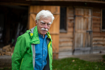 Portrait of a handsome senior man wearing a casual green jacket next to his cottage house in the...