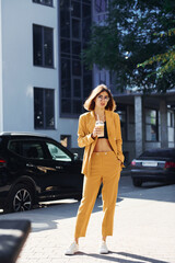 Obraz premium Coffee break. Young fashionable woman in burgundy colored coat at daytime with her car