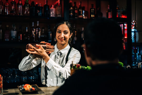 Cheerful bartender mixing cocktail near client