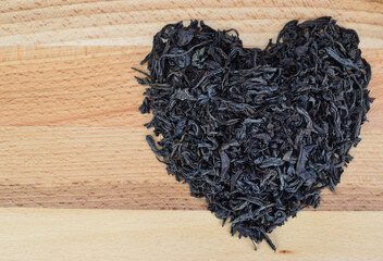 A handful of large leaf black tea laid out in the shape of a heart on a wooden surface.