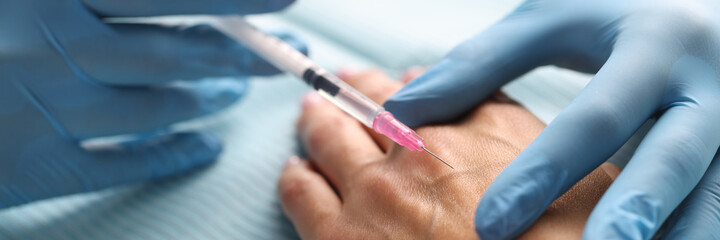 Gloved doctor injects patient into skin of hands.