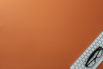 Glasses and keyboard on orange background