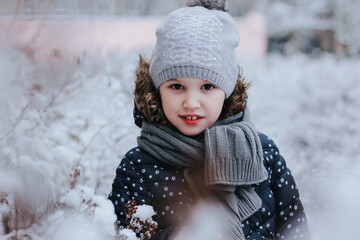 Little girl playing among the bushes covered with snow. First snow. Wintertime, christmas, new year, holidays concept.