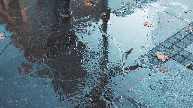 female feet walking on city street pool or puddle in waterproof shoes. Woman having fun splasing water at rainy wet weather. Playful carefree girl enjoying urban spring in rubber boots. Concept of joy