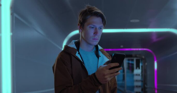 Portrait of handsome young man in urban city scene, screen lit with neon lights and smartphone device. Concept serious worried millennial generation z man in futuristic space surroundings