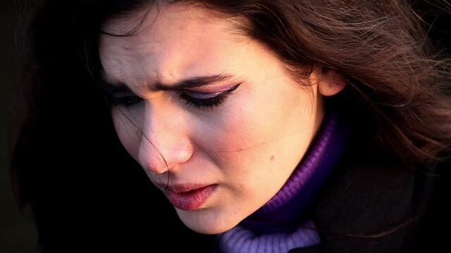 Ein Close-Up einer jungen Frau mit dunklen Haaren und lila Make-Up. Sie ist sehr traurig und fast am weinen.