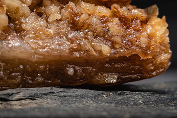 primer plano macro de baklava pastel típico y tradicional turco masa hojaldrada y nuez y pistacho triturado con miel y almíbar de azúcar sobre plato de piedra laja negra