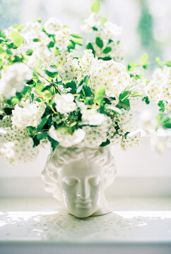 tree branches with white flowers in a vase with a face of apollo