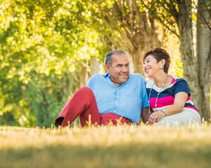 Older Hispanic couple sitting in grassy field