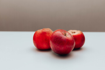 Three red juicy apples on white table against brown background. Space for text