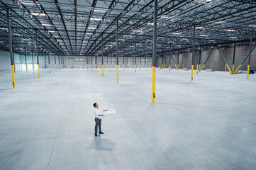 Indian architect holding blueprint in empty warehouse