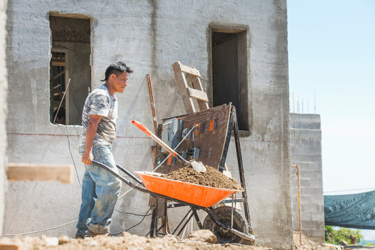 Hispanic Construction Worker Pushing Wheelbarrow At Construction Site