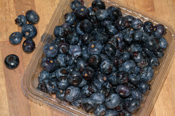Blaubeeren in einer Kunststoffverpackung auf einem Holzbrett.