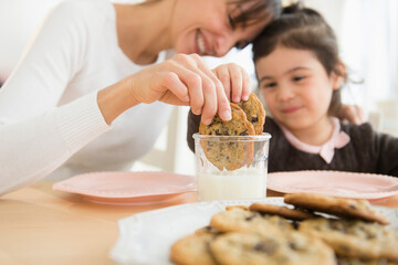 Hispanic mother and daughter dunking cookies in milk