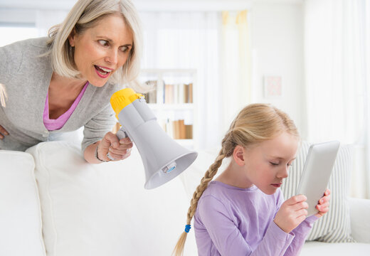 Senior Caucasian Woman Yelling In Megaphone At Granddaughter