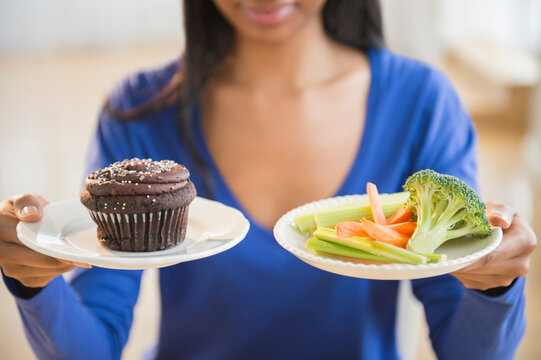 Mixed race woman choosing vegetables or cupcake