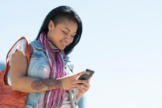 Mixed race woman using cell phone under blue sky