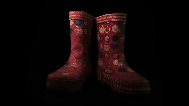 Old kids pink rain rubber boots rotate on a black background in the loop
