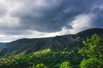 Fototapeta na wymiar Village view on mountain foothills on a dark cloudy day.