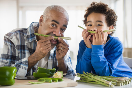 Mixed race grandfather and grandson making mustaches with asparagus